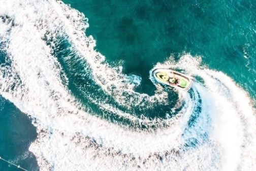 Aerial view of jet ski making a circular wave pattern in clear blue water.