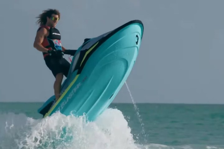 Person riding a blue jet ski, catching air above ocean waves under clear sky.