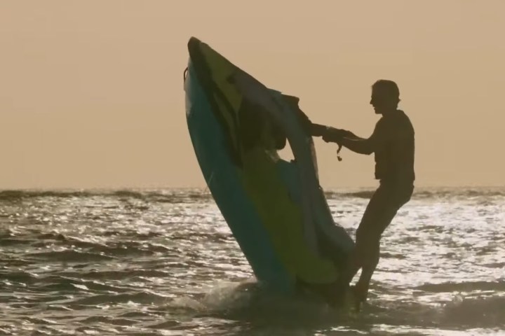 Silhouette of person riding a jet ski, performing a vertical jump in the ocean at sunset.