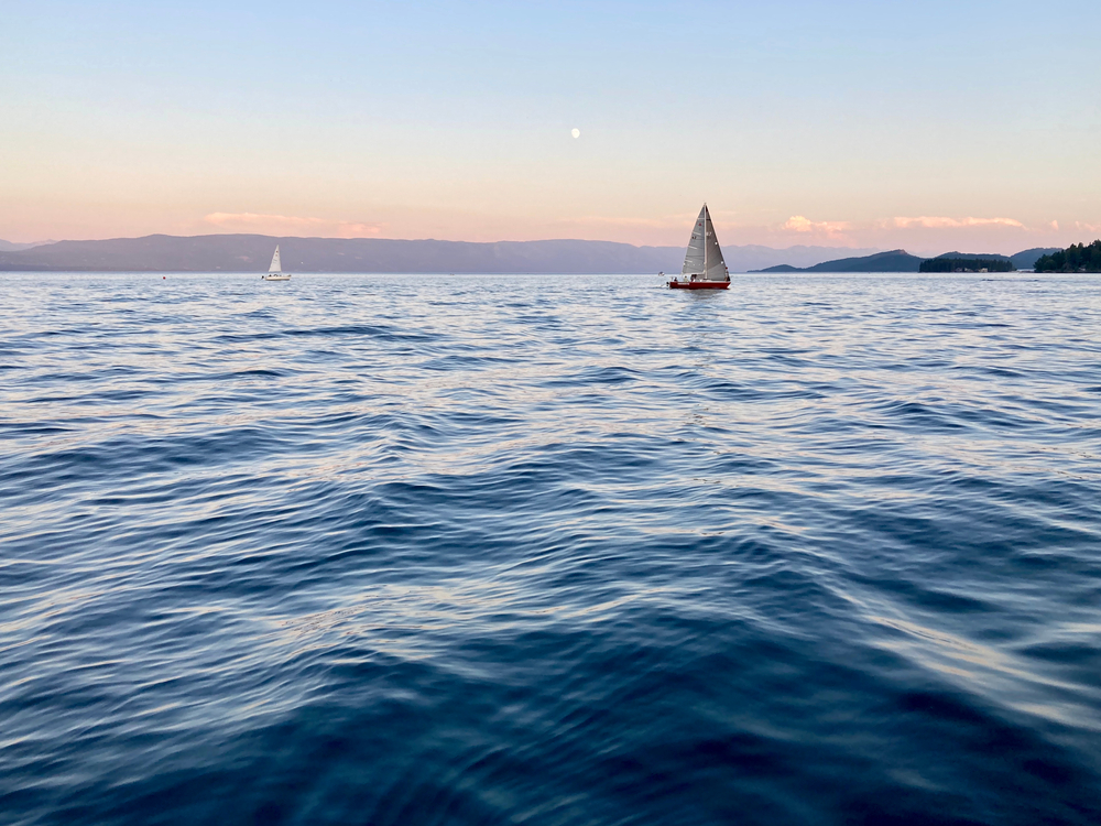 Sailboats on a calm lake at sunset with mountains in the distance.