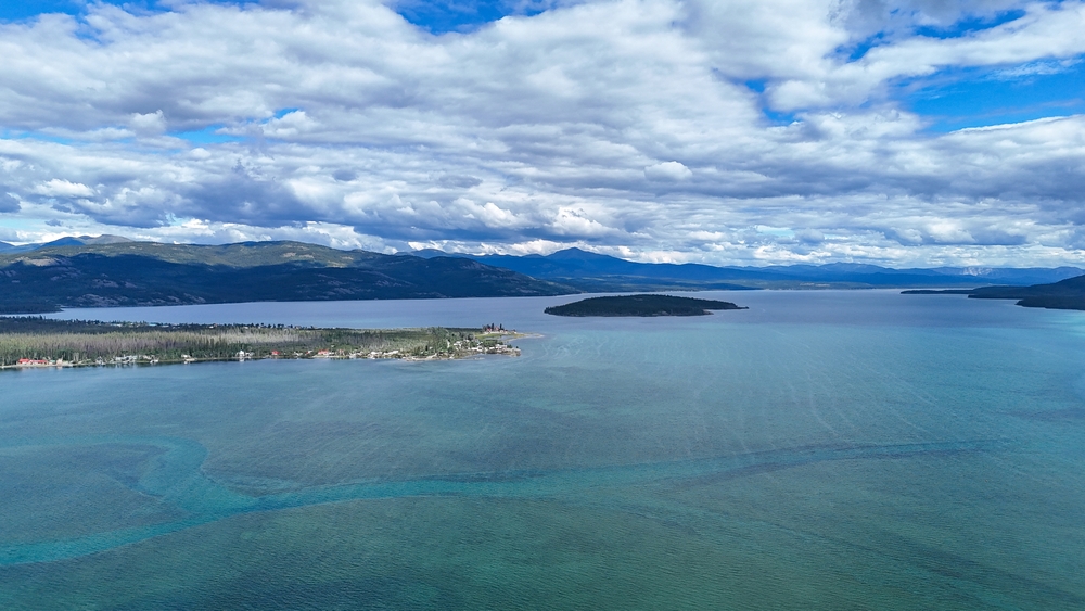 Aerial view of a large lake with islands and distant mountains under a cloudy sky.